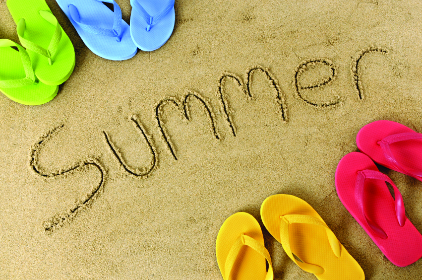The word summer written in sand with selection of flip flops (studio shot - directional lighting and warm color cast are intentional).
